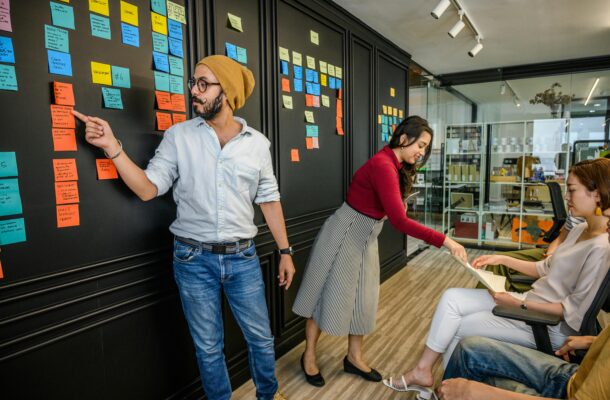 Team members collaborating in a modern office with sticky notes on a wall, focusing on brainstorming and strategy.