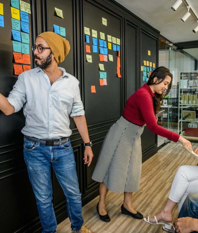 Team members collaborating in a modern office with sticky notes on a wall, focusing on brainstorming and strategy.